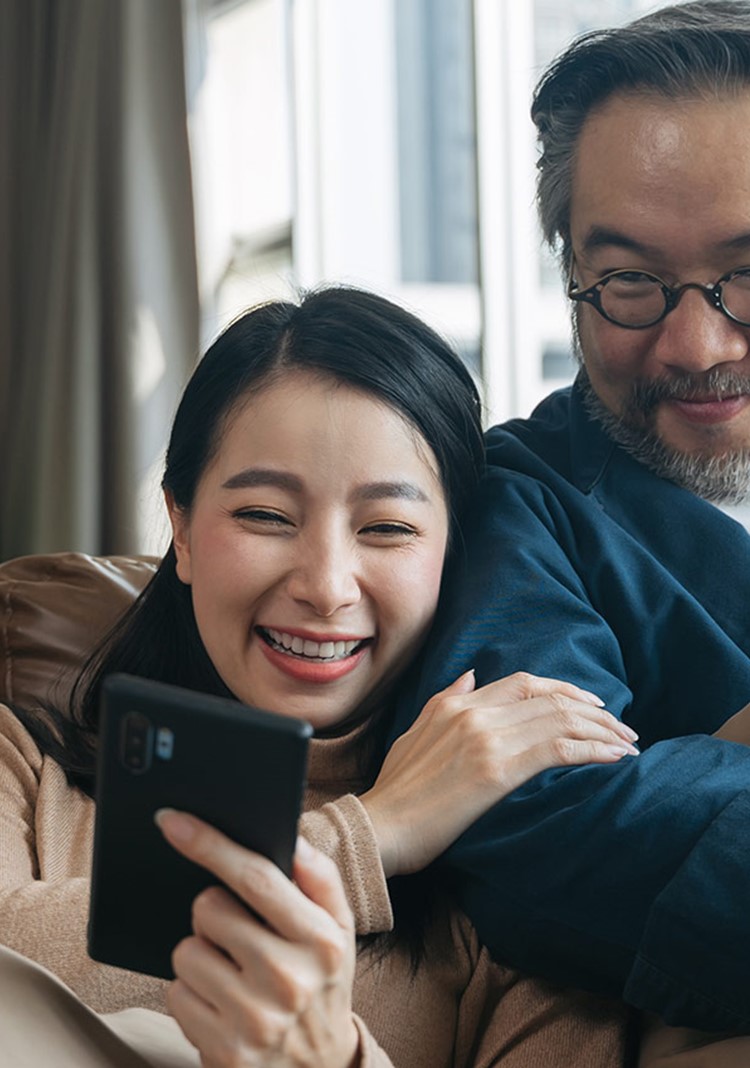 Asian Female Showing Smartphone To Husband In Living Room At Home