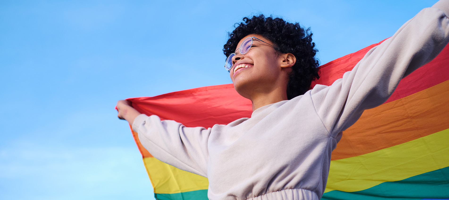 An African American Young Woman Holding And Raising A Rainbow Flag Over The Blue Sky