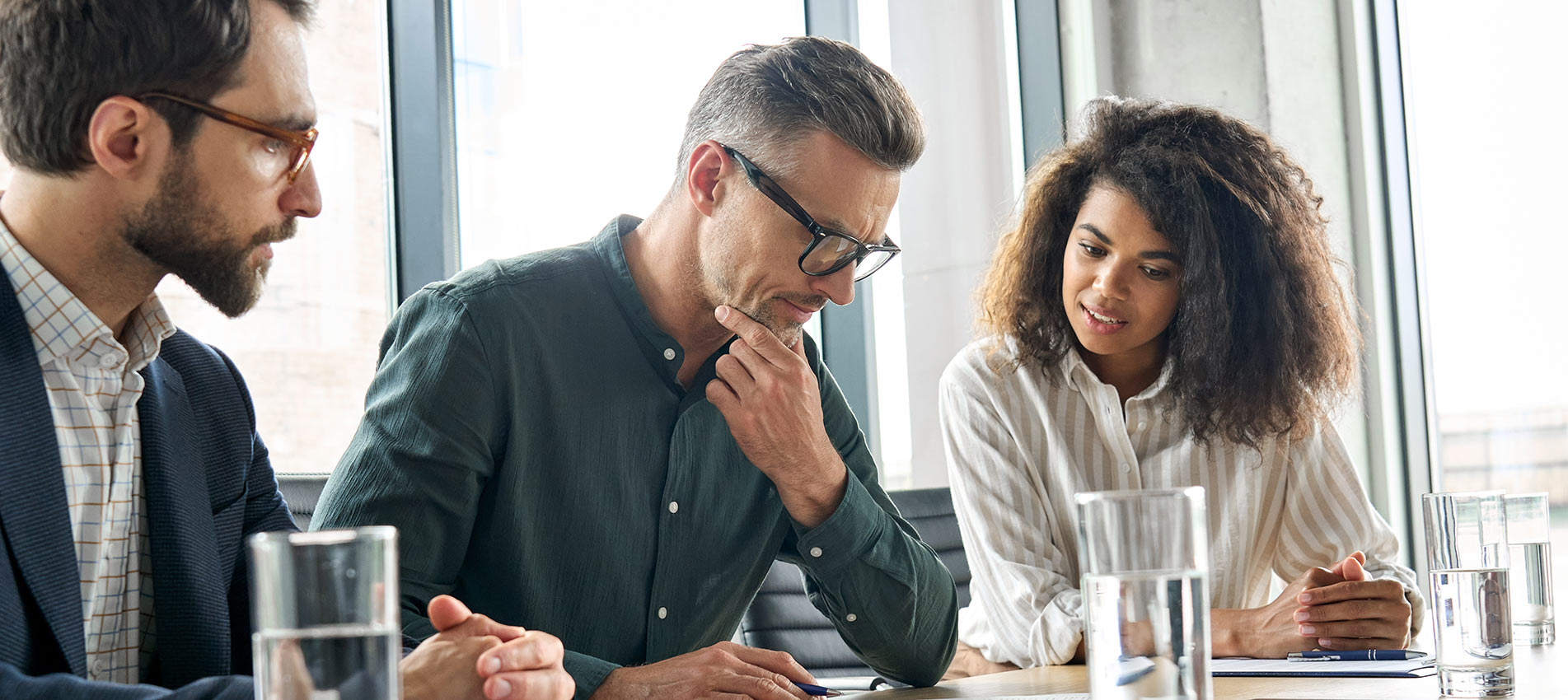 Focused Mature Businessman Reading Contract Considering Risks With Lawyers