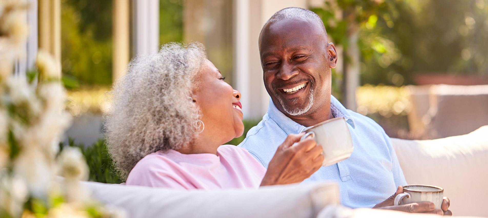 Retired Couple Sitting Outdoors At Home Having Morning Coffee Togethe
