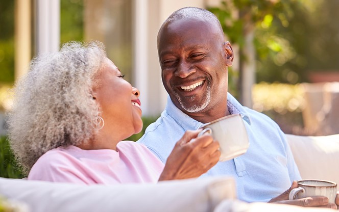 Retired Couple Sitting Outdoors At Home Having Morning Coffee Togethe