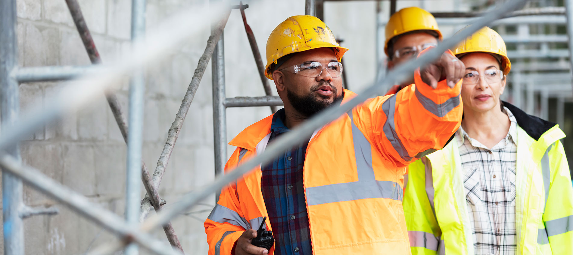 Woman Two Men Walk Under Scaffold At Construction Site