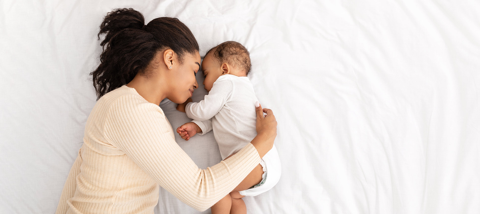 African Mother Hugging Sleeping Baby Lying In Bed Indoor