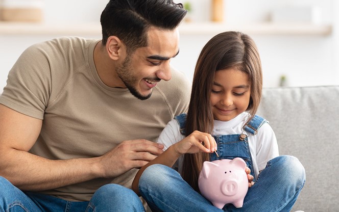 Little Girl And Dad Saving Money In Piggy Bank