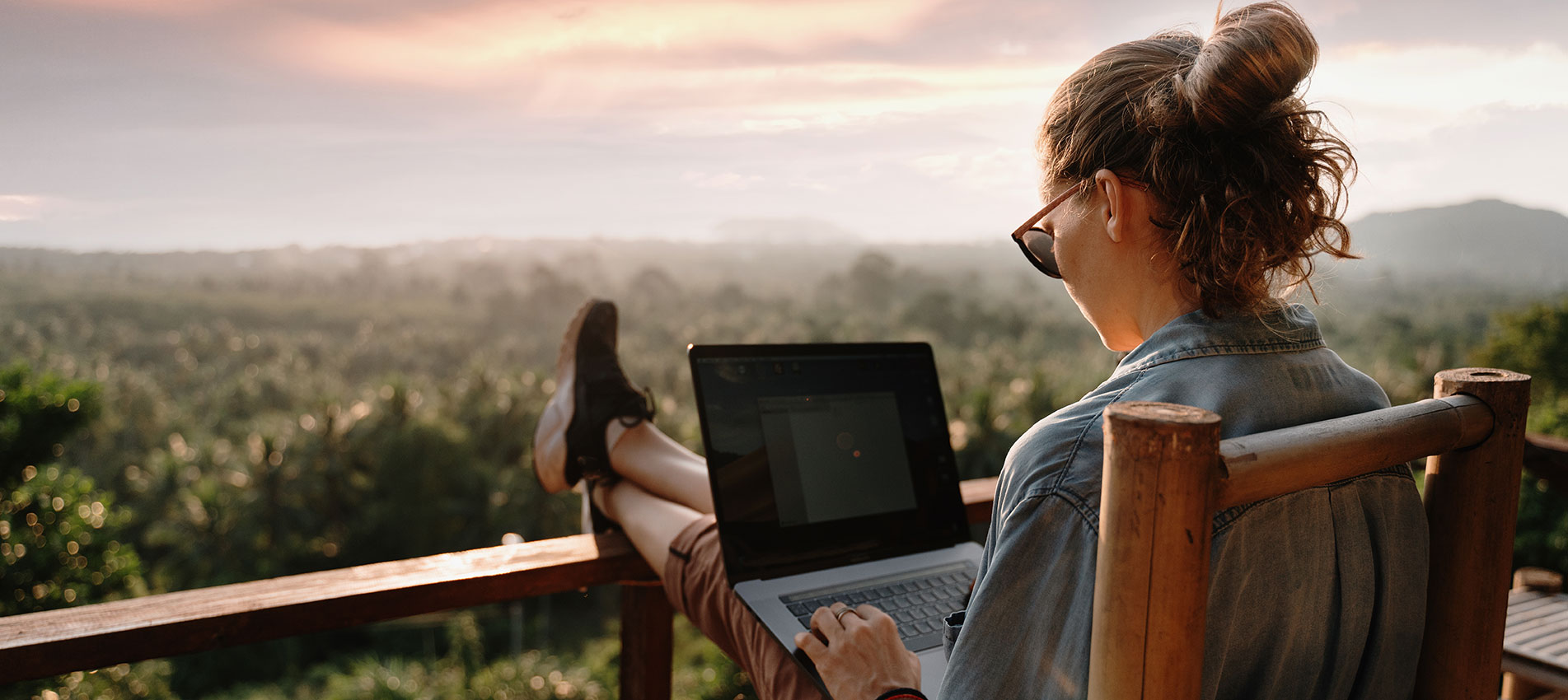 Young Businesswoman Working On A Laptop At Sunrise On The Top Of The Mountain