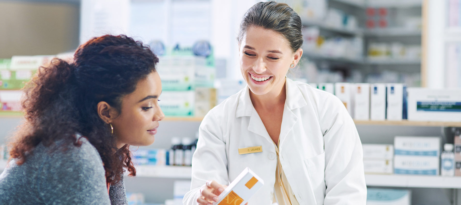 Young Pharmacist Using A Digital Tablet While Assisting A Customer In A Chemist