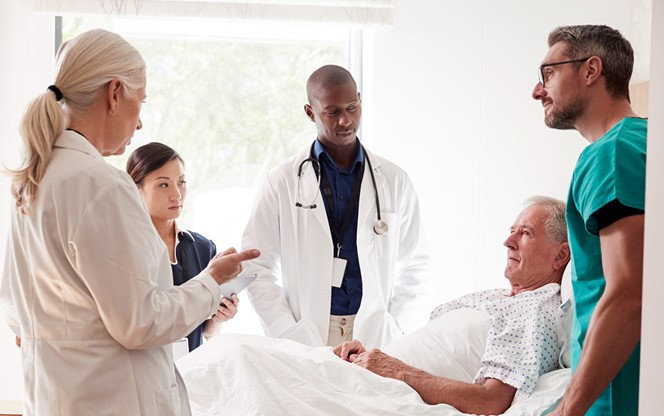 Medical Team On Rounds Meeting Around Bed Of Senior Male Patient