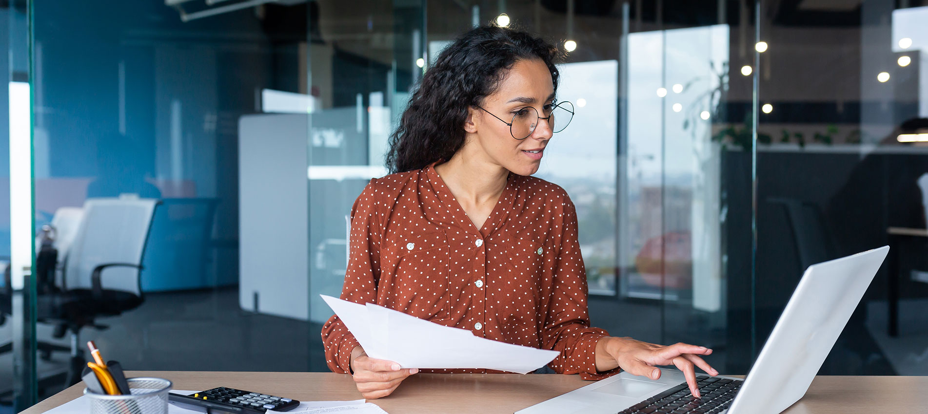 Hispanic Woman With Laptop Looking At Bills And Contracts