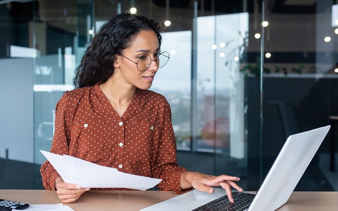 Hispanic Woman With Laptop Looking At Bills And Contracts