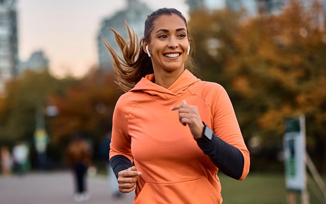 Happy Sportswoman With Earbuds Running In The Park