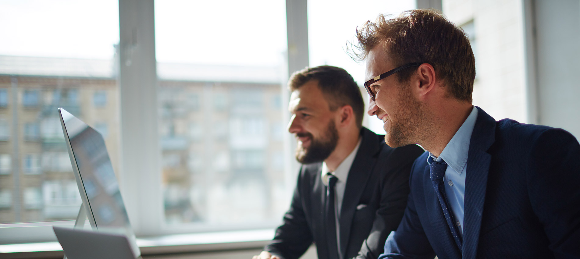 Smiling Businessman And His Colleague Looking At Computer Monitor At Meeting