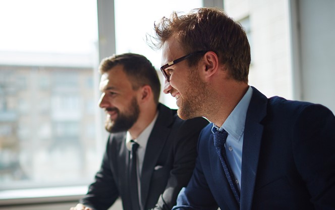 Smiling Businessman And His Colleague Looking At Computer Monitor At Meeting