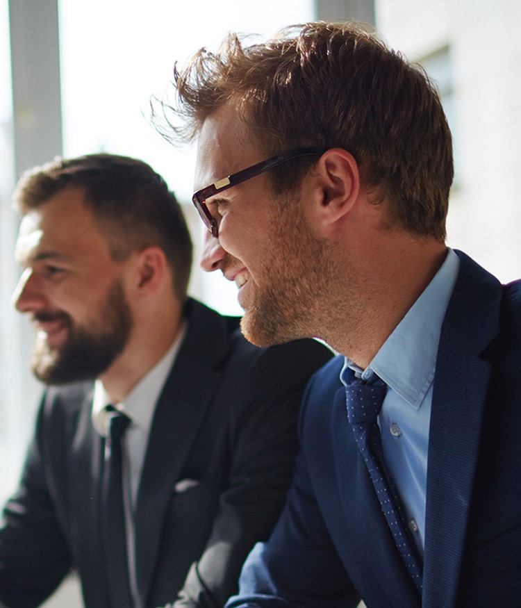 Smiling Businessman And His Colleague Looking At Computer Monitor At Meeting