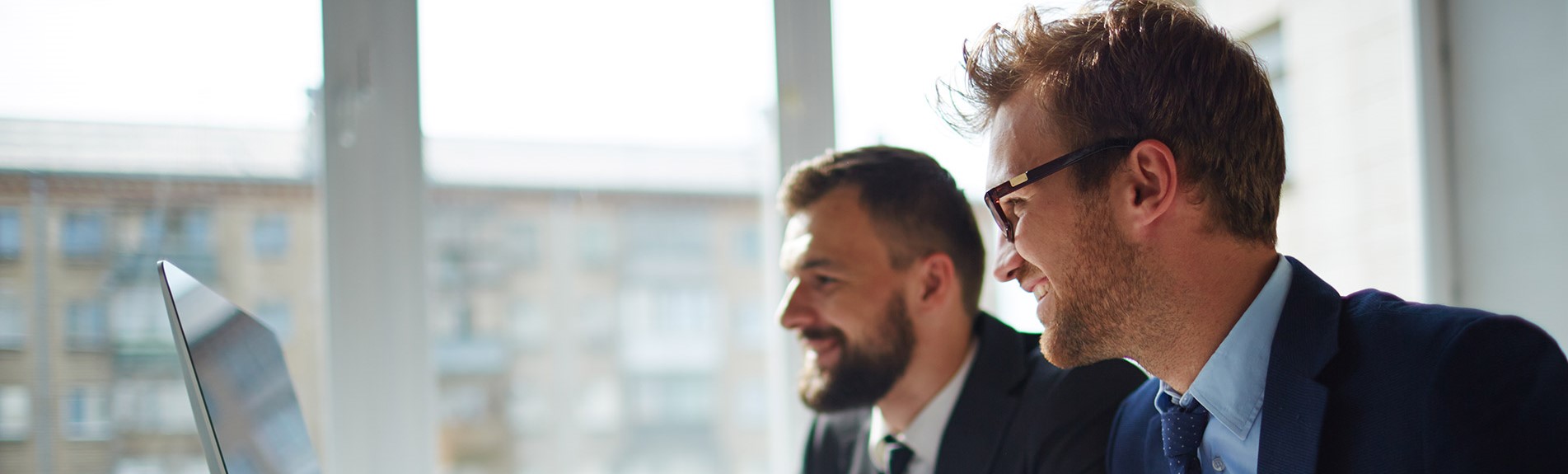 Smiling Businessman And His Colleague Looking At Computer Monitor At Meeting