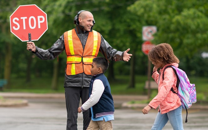 Smiling Crossing Guard Helps Students Safely Cross Street
