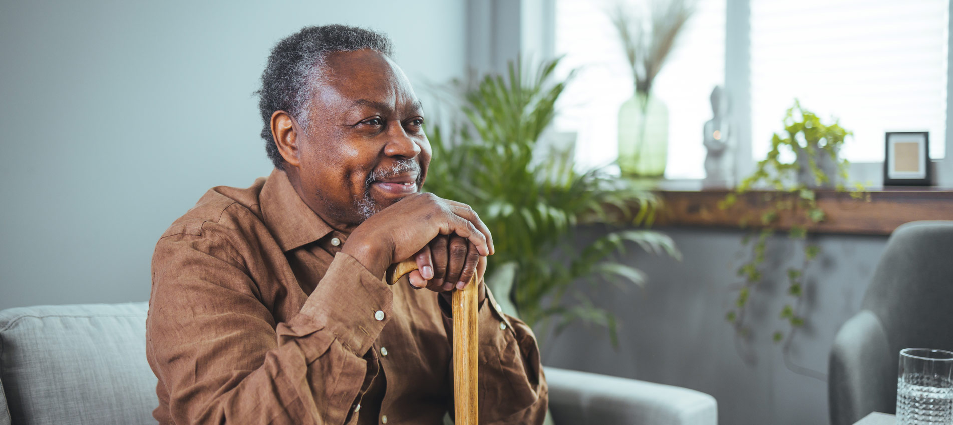 Thoughtful Elderly Man Sitting Alone At Home With His Walking Cane