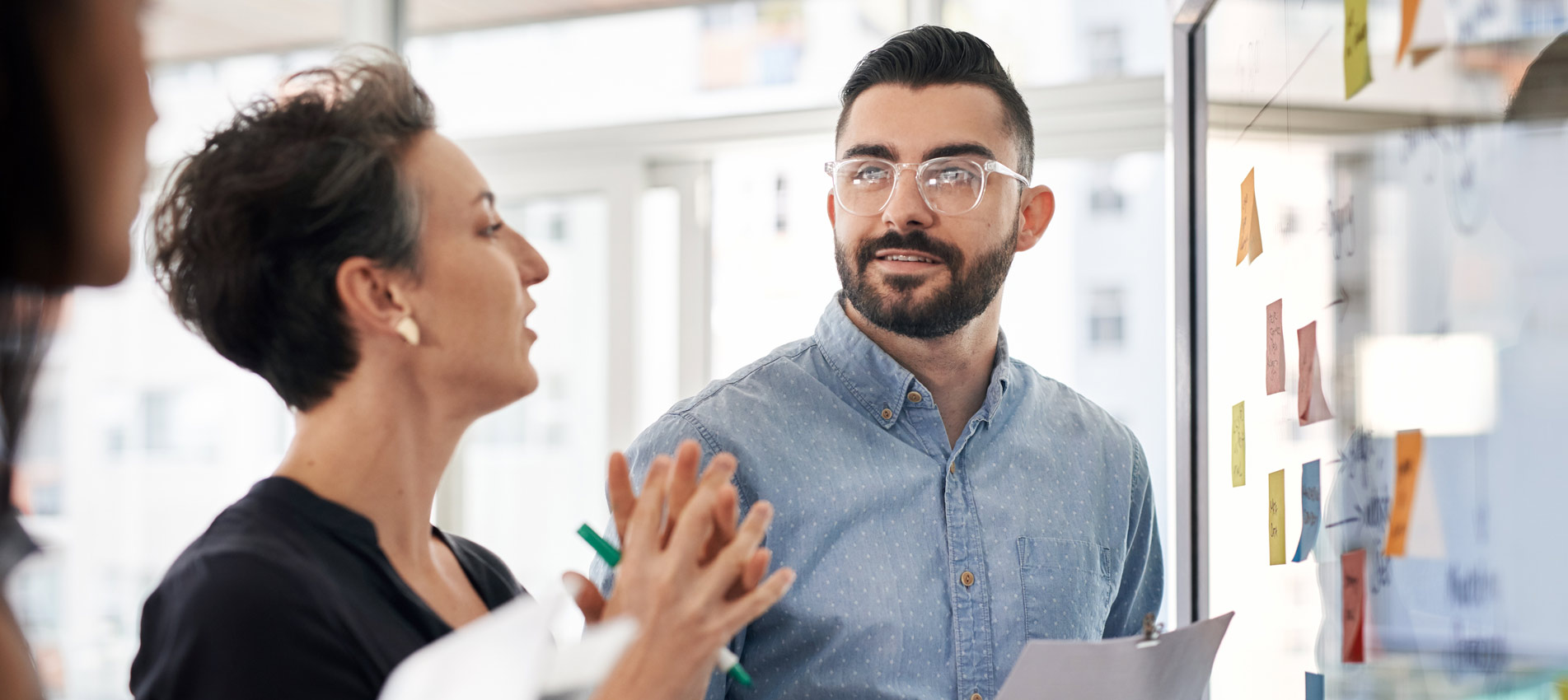 Businesspeople Brainstorming Ideas And Writing Notes On A Glass Wall In A Modern Office
