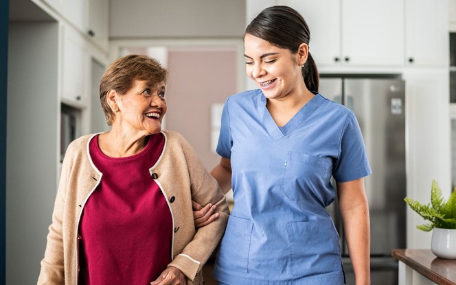 Home Caregiver Helping Senior Woman To Walk At House
