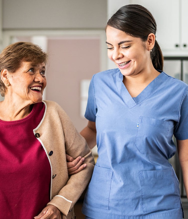 Home Caregiver Helping Senior Woman To Walk At House