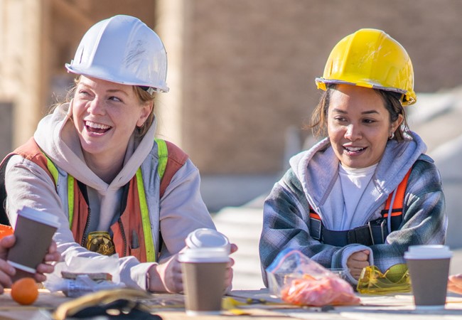 Two Female Construction Workers On A Lunch Break With Colleagues