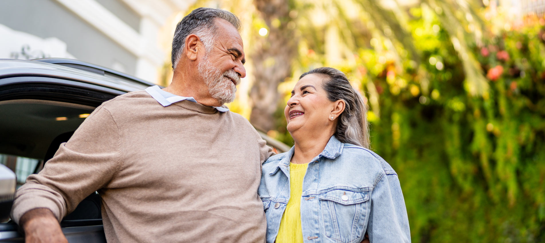 Happy Hispanic Senior Couple Standing Next To A Car At New House