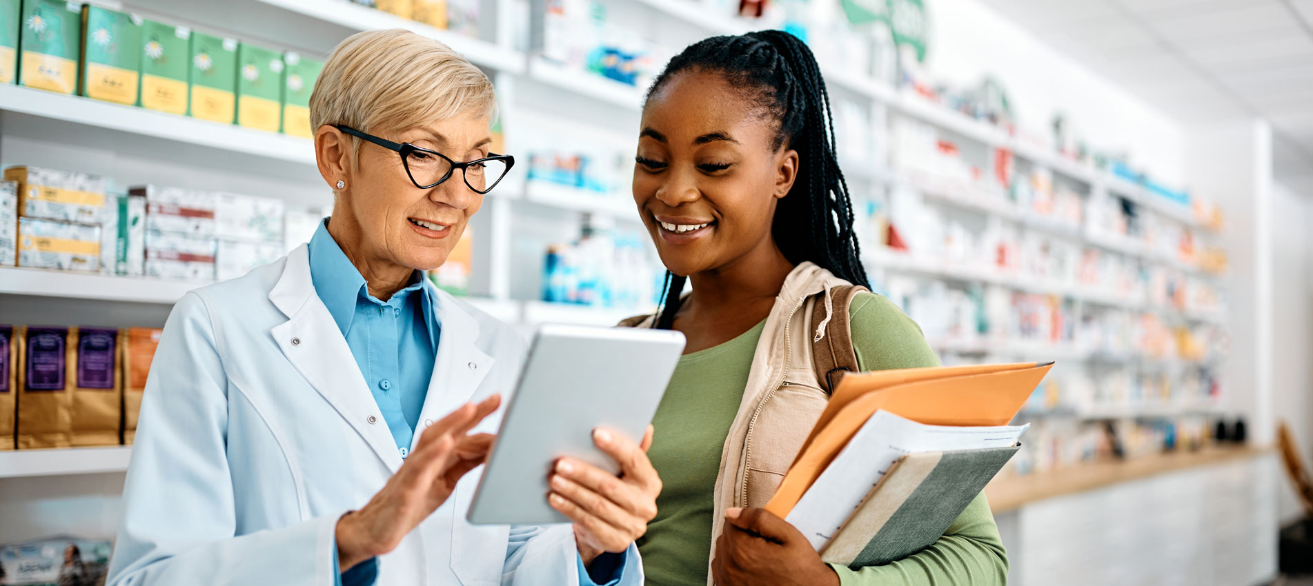 Senior Pharmacist And Young Black Woman Using Touchpad In A Pharmacy