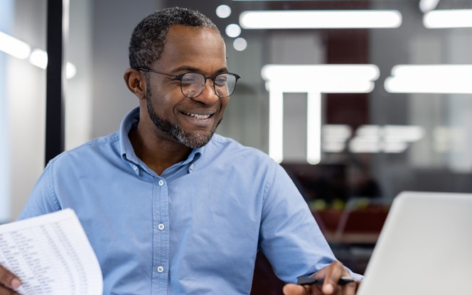 African American Businessman Smiling While Analyzing Graphs On Laptop