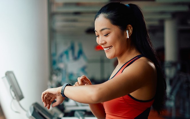 Asia Athletic Woman Using Fitness Tracker While Running On Treadmill In A Gym