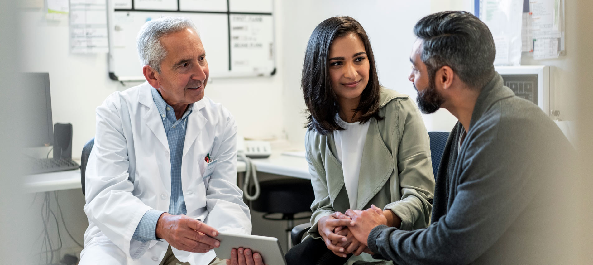 Doctor Holding A Digital Tablet Discussing Fertility Benefits With Couple