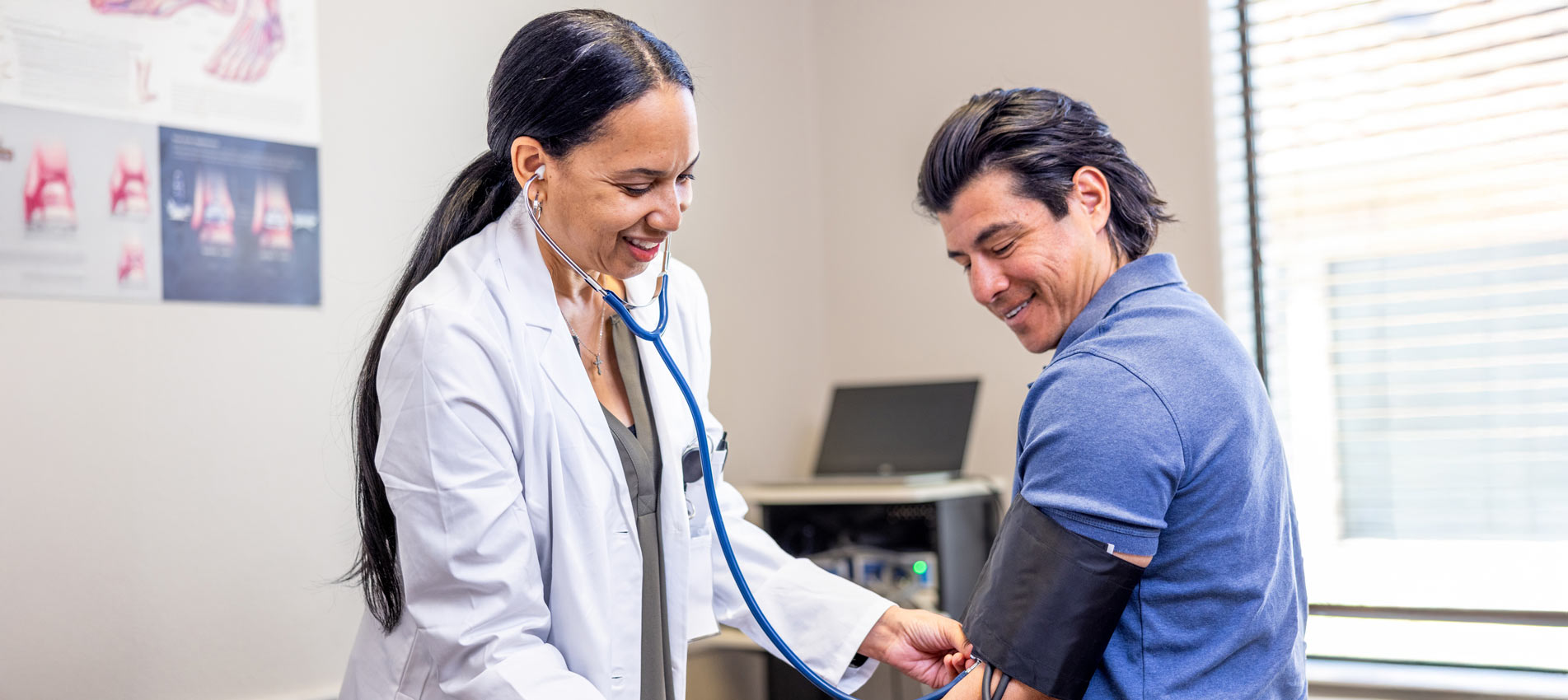 Hispanic Male At A Doctors Appointment With A Black Female Doctor Checking Blood Pressure