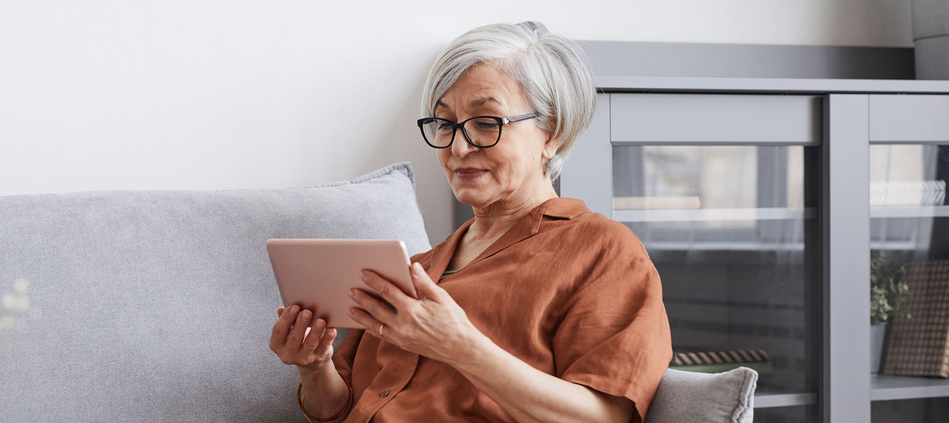 Senior Woman Using Digital Tablet While Lying On Couch At Home