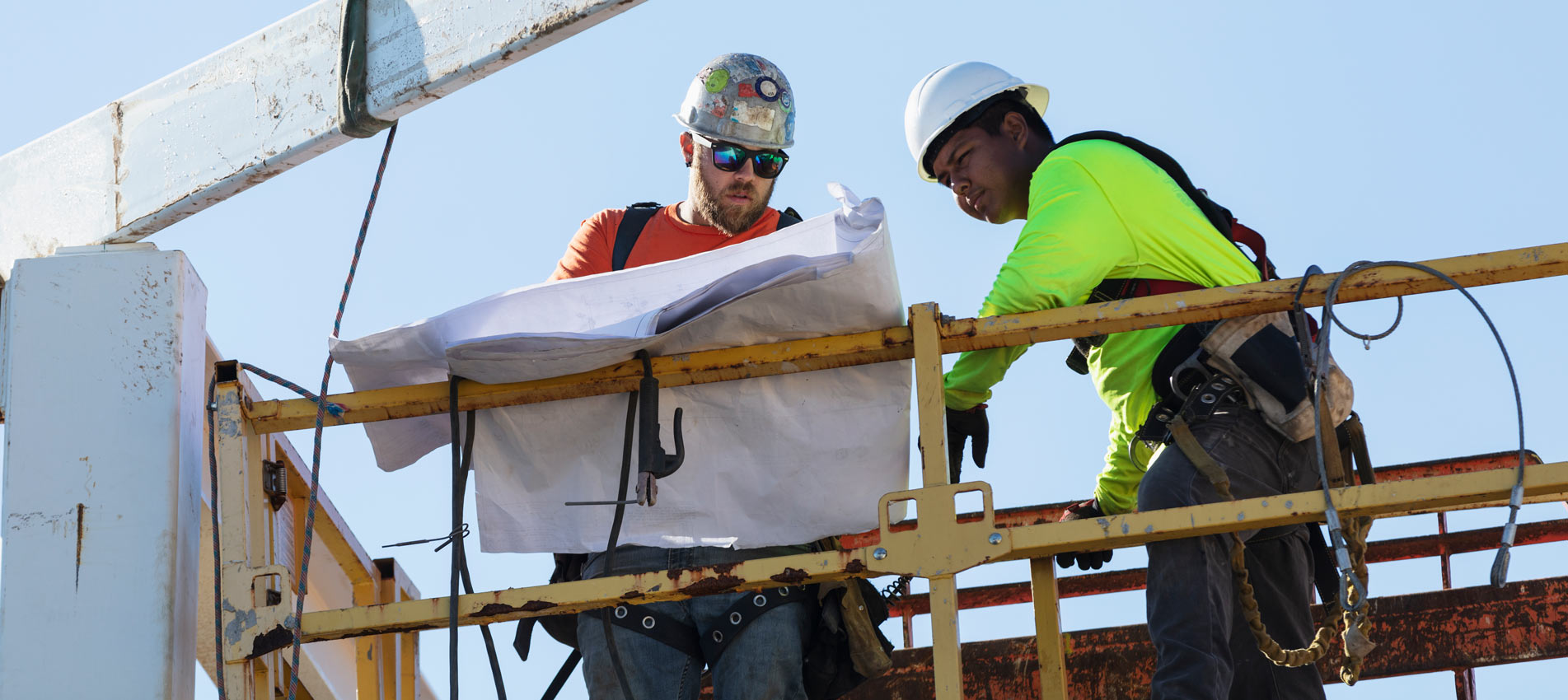 Two Ironworkers On Construction Platform With Blueprints