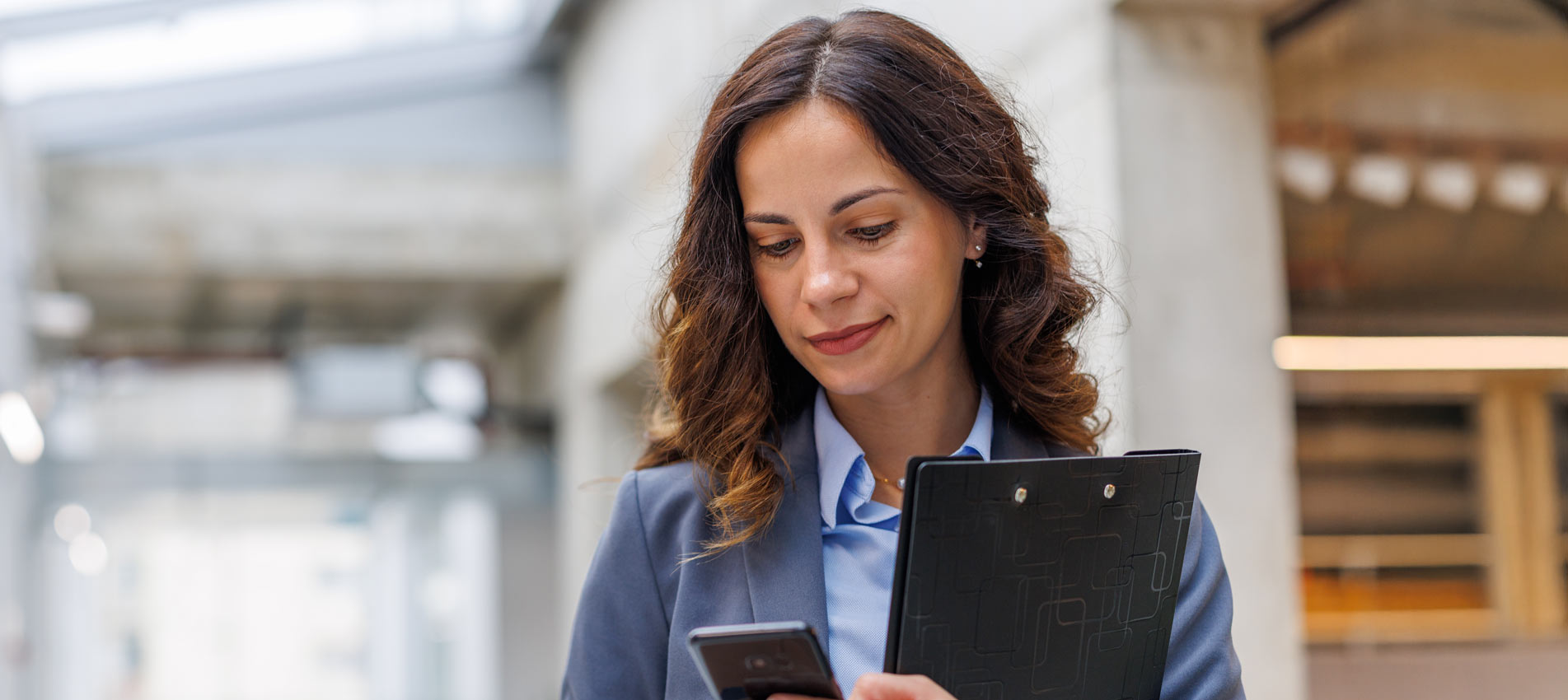 Businesswoman Checking Smartphone While Walking In Office