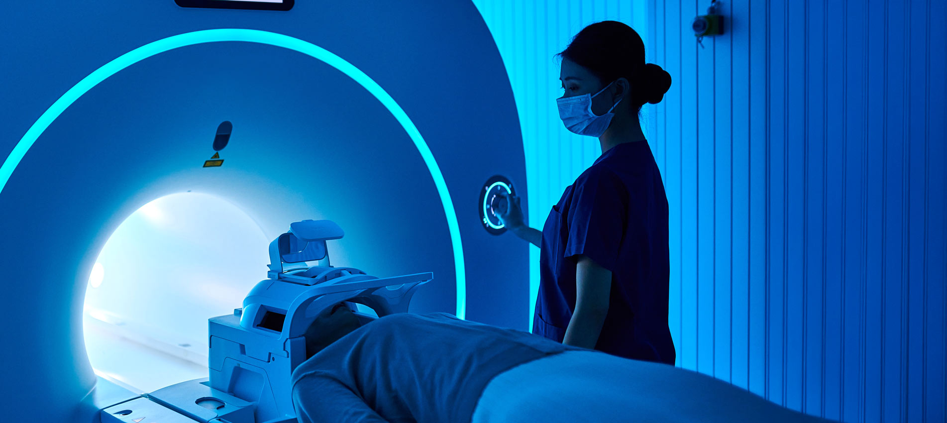 Female Nurse Operating MRI Scan Machine At MRI Scanner Room