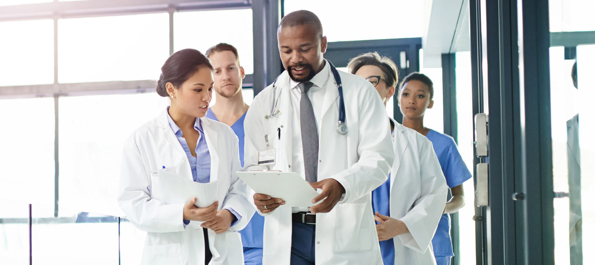 Group Of Doctors Discussing A Patients File While Walking Through A Medical Center