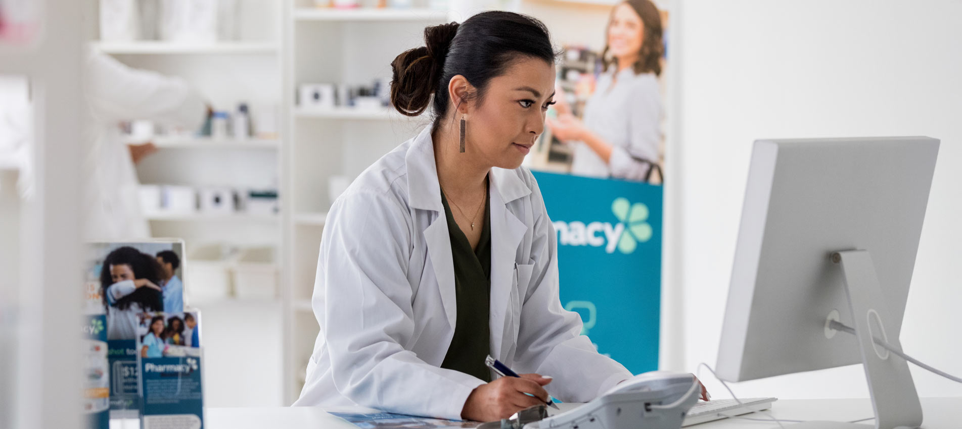 Asian Female Pharmacist Uses Computer To Check Inventory For A Drug